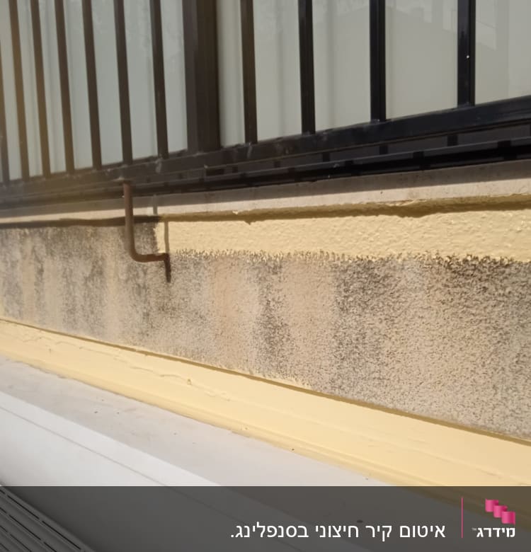 קיר עם איטום צהוב מתחת לחלון עם סורגים.